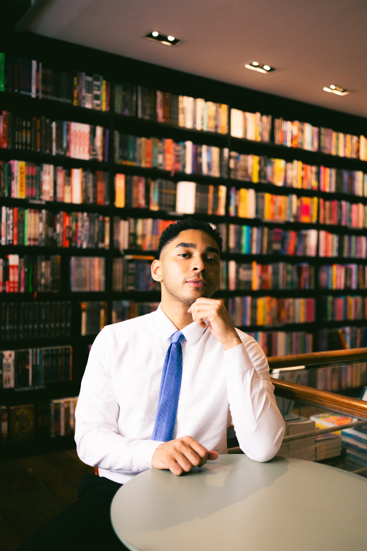 Douglas Aleixo pensativo em uma mesa de biblioteca